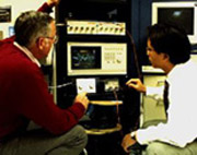 Dr. Robert Scholtz and graduate student Moe Win review the signal from the impulse radio on an oscilliscope.